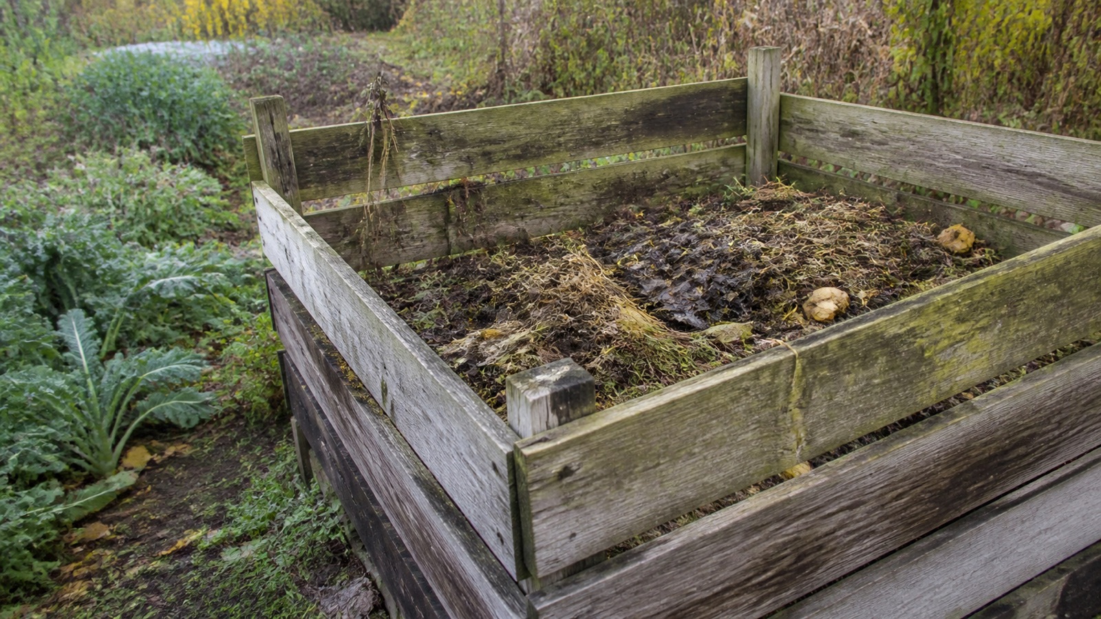 A weathered wooden compost bay in an established Vermont garden — about Vermont Composting
