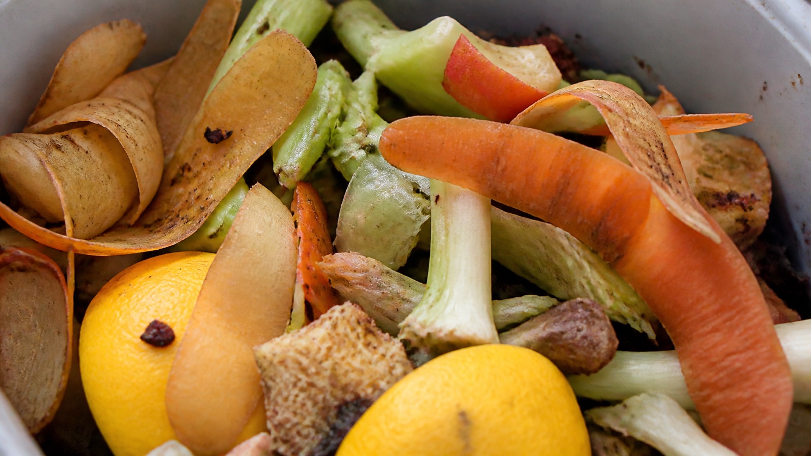 Extreme close-up filling the frame: vegetable peelings and fruit scraps in a kitchen compost caddy, compost fruit