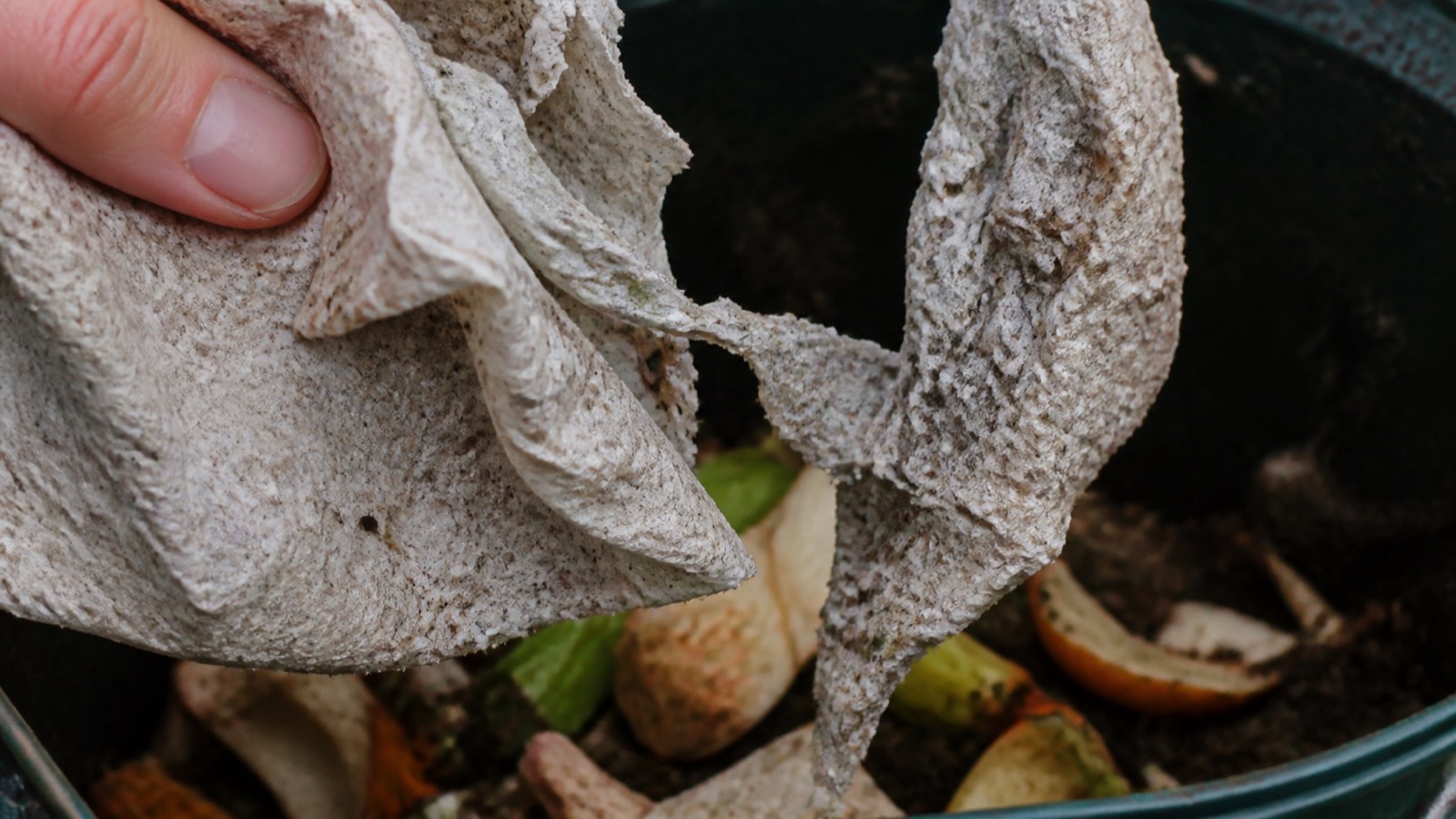 Extreme close-up filling the frame: used kitchen paper being torn and added to a compost caddy, compost paper towels