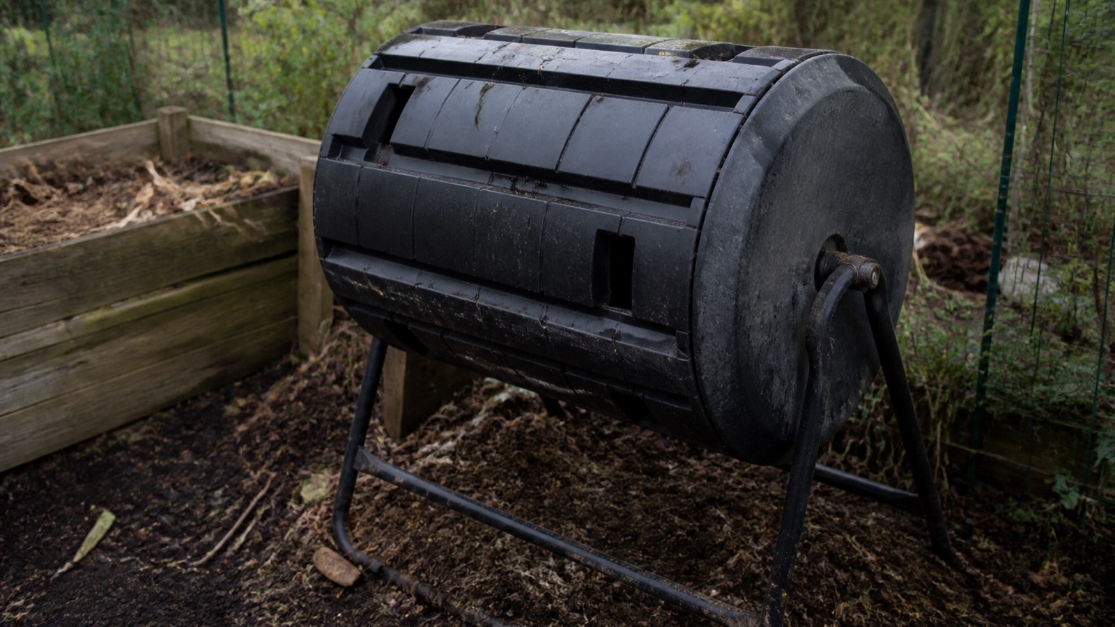 A black rotating compost tumbler on a metal frame in a garden, compost tumbler